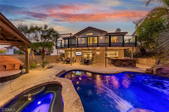 back house at dusk featuring a patio area, outdoor lounge area, a balcony, an in ground hot tub, and a bar