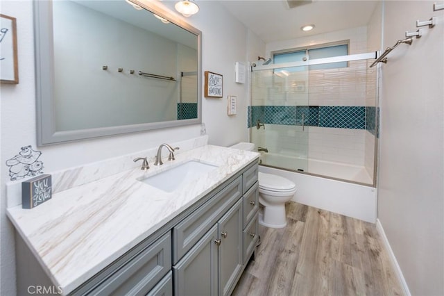 full bathroom featuring toilet, vanity, hardwood / wood-style floors, and bath / shower combo with glass door