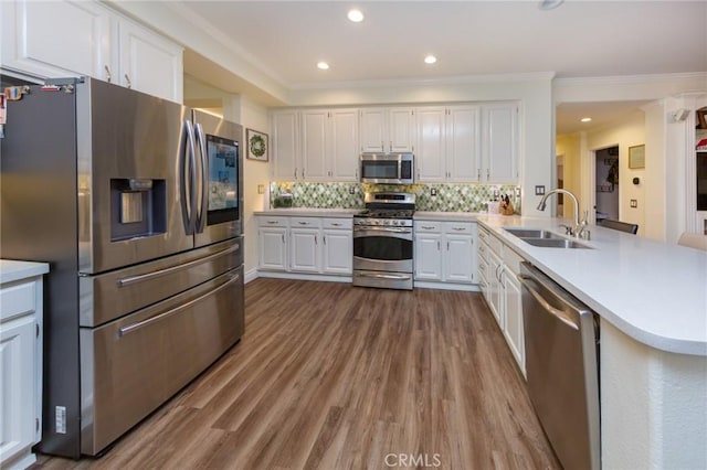 kitchen with sink, stainless steel appliances, kitchen peninsula, white cabinets, and decorative backsplash