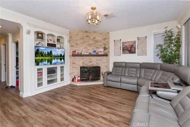 living room featuring hardwood / wood-style floors, built in shelves, a stone fireplace, and ornamental molding