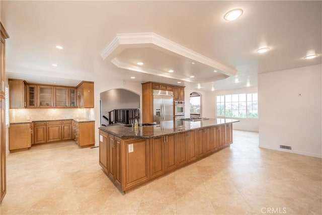 kitchen featuring a spacious island, sink, dark stone countertops, appliances with stainless steel finishes, and tasteful backsplash