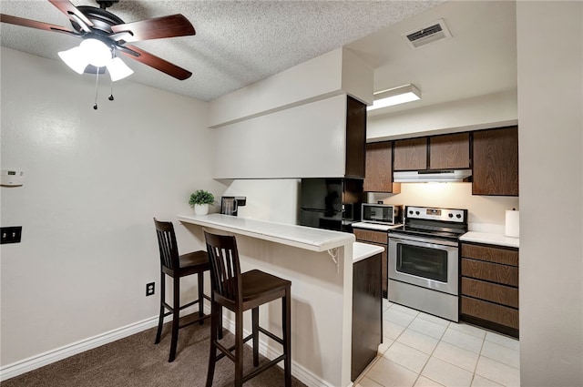 3504 Rainbow Ln, Highland, CA 92346 - kitchen with stainless steel electric stove, under cabinet range hood, freestanding refrigerator, a breakfast bar, and a peninsula