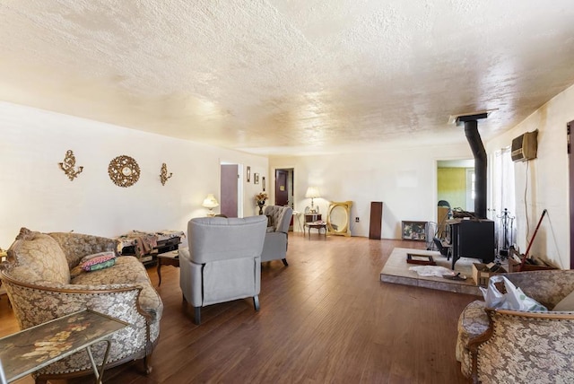 living room with a wall mounted air conditioner, wood-type flooring, a wood stove, and a textured ceiling