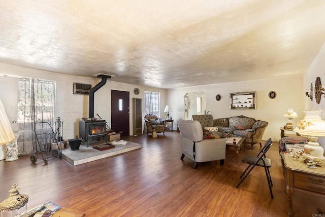 living room with a wall unit AC, a wood stove, dark wood-type flooring, and a textured ceiling