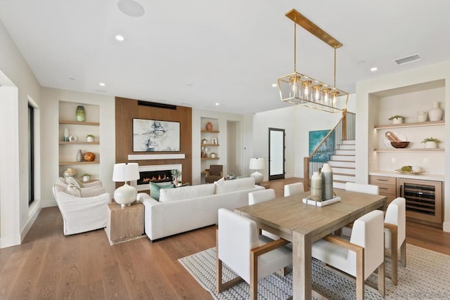 dining space with an inviting chandelier, built in features, beverage cooler, and light hardwood / wood-style flooring