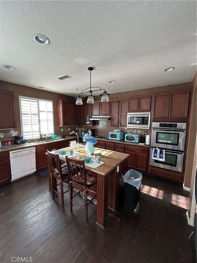 kitchen featuring a center island, dark hardwood / wood-style floors, a textured ceiling, appliances with stainless steel finishes, and decorative light fixtures