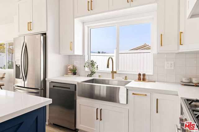 kitchen featuring appliances with stainless steel finishes, backsplash, sink, white cabinets, and light hardwood / wood-style floors