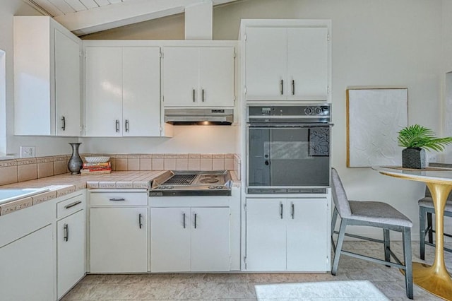 kitchen with stainless steel gas cooktop, vaulted ceiling, black oven, and white cabinetry