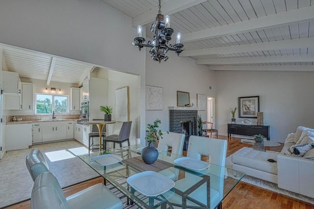 dining room featuring beamed ceiling, a fireplace, a chandelier, light hardwood / wood-style flooring, and sink