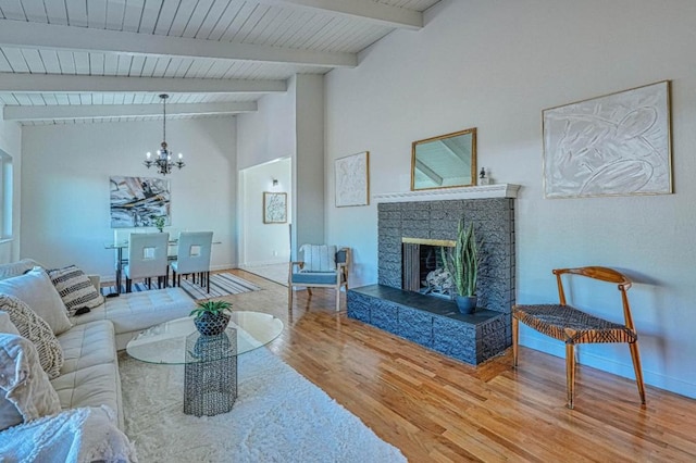 living room featuring hardwood / wood-style floors, a tile fireplace, vaulted ceiling with beams, and an inviting chandelier