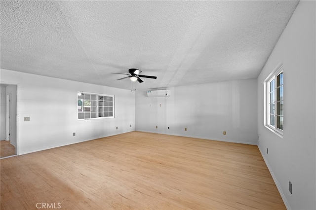 empty room with ceiling fan, light hardwood / wood-style floors, an AC wall unit, and a textured ceiling