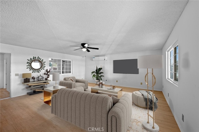 living room featuring ceiling fan, light wood-type flooring, a textured ceiling, and a wall unit AC