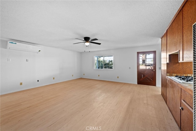 unfurnished living room featuring ceiling fan, a textured ceiling, a wall unit AC, and light hardwood / wood-style flooring