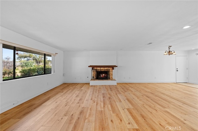 unfurnished living room with light wood-type flooring, a fireplace, and an inviting chandelier