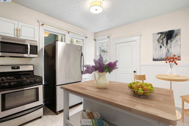 kitchen featuring wood walls, wooden counters, white cabinets, a textured ceiling, and stainless steel appliances