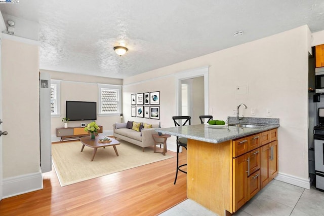 kitchen featuring a kitchen bar, kitchen peninsula, light wood-type flooring, a textured ceiling, and sink