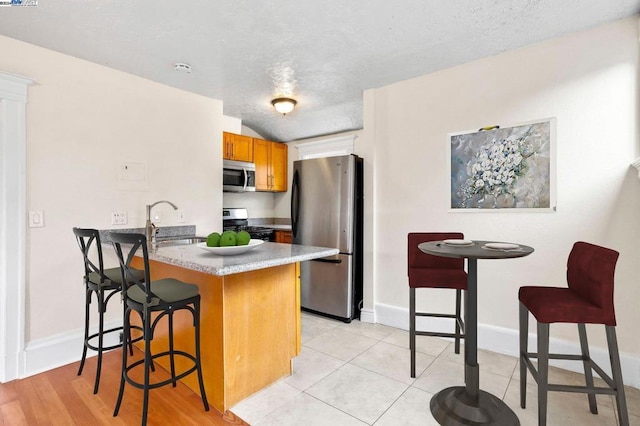 kitchen with sink, stainless steel appliances, kitchen peninsula, light hardwood / wood-style floors, and a breakfast bar