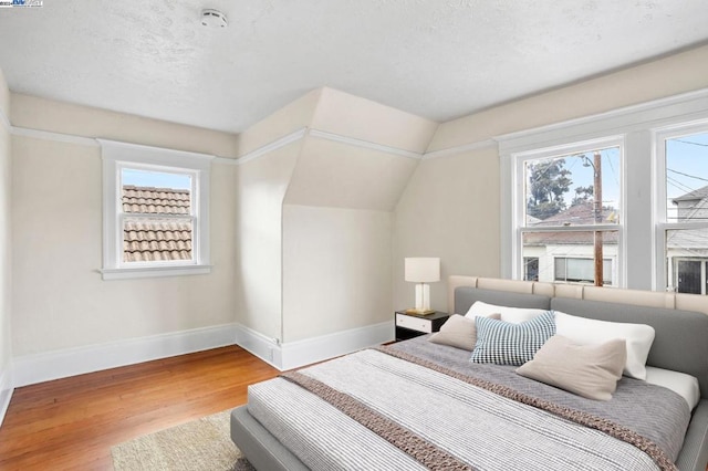 bedroom with hardwood / wood-style floors, a textured ceiling, and vaulted ceiling