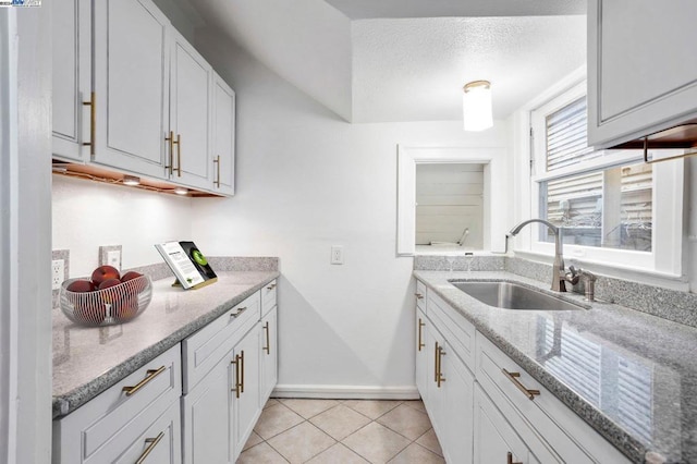 kitchen with a textured ceiling, light tile patterned flooring, white cabinetry, and sink