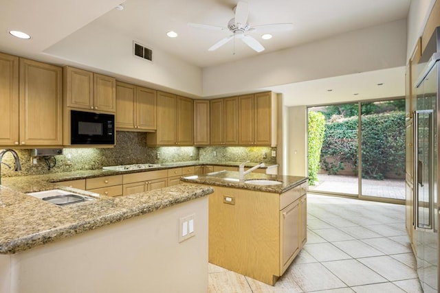 kitchen featuring light stone countertops, tasteful backsplash, black microwave, sink, and an island with sink