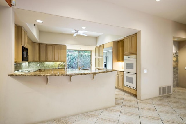 kitchen featuring built in appliances, decorative backsplash, light stone countertops, kitchen peninsula, and a breakfast bar area