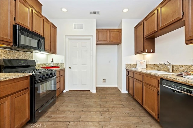 kitchen featuring sink, light wood-type flooring, light stone counters, and black appliances