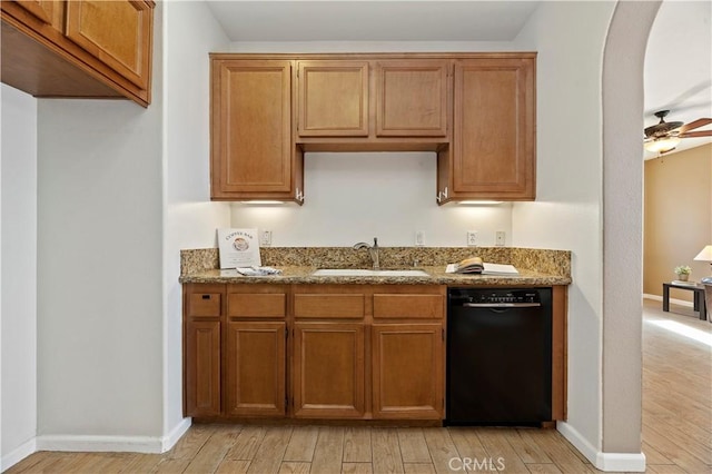 kitchen with stone counters, sink, ceiling fan, black dishwasher, and light wood-type flooring