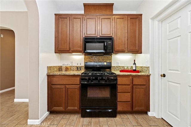 kitchen featuring black appliances, light stone counters, and light hardwood / wood-style flooring