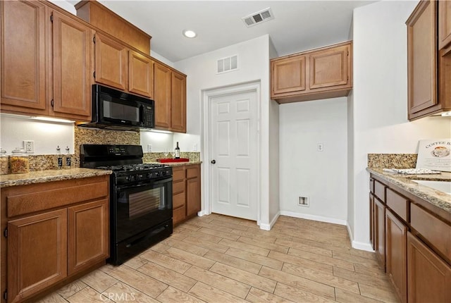 kitchen featuring black appliances, light stone counters, and light wood-type flooring