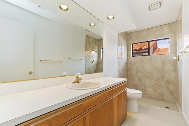 bathroom featuring a tile shower, vanity, and toilet