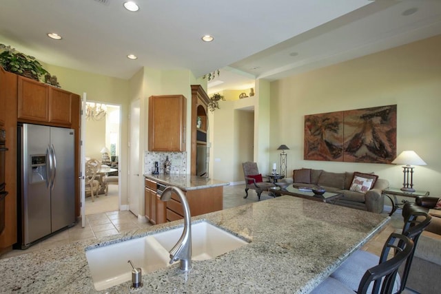 kitchen with kitchen peninsula, stainless steel refrigerator with ice dispenser, decorative backsplash, light stone counters, and a breakfast bar area