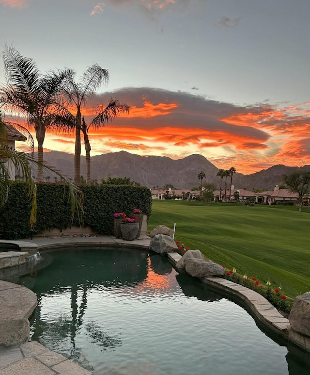 pool at dusk featuring a lawn and a mountain view