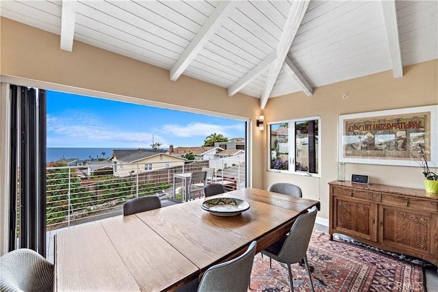 dining space with vaulted ceiling with beams and a water view