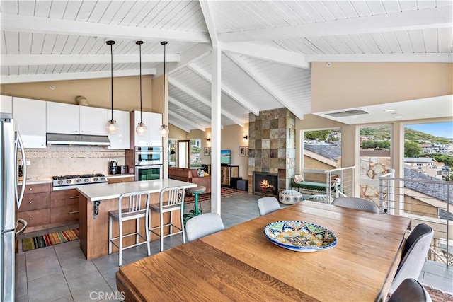 dining area featuring beam ceiling, high vaulted ceiling, and a tiled fireplace