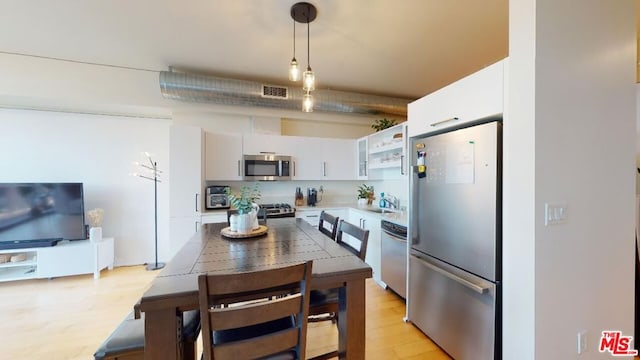 kitchen with decorative light fixtures, sink, white cabinetry, light wood-type flooring, and appliances with stainless steel finishes