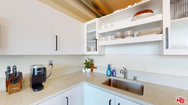 kitchen featuring light stone countertops, white cabinetry, and sink