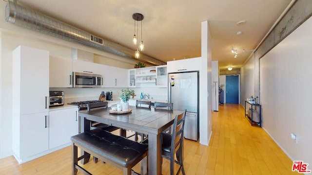 kitchen featuring appliances with stainless steel finishes, pendant lighting, light hardwood / wood-style floors, and white cabinets