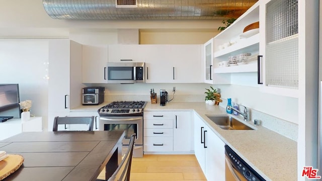 kitchen featuring light stone countertops, white cabinets, stainless steel appliances, sink, and light hardwood / wood-style flooring