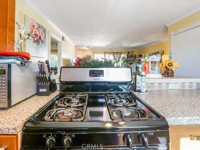 kitchen with black gas range oven, light stone counters, and ornamental molding