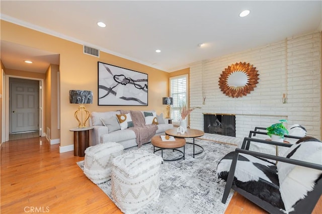 living room featuring crown molding, light hardwood / wood-style floors, and a brick fireplace