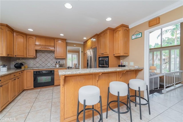 kitchen with black appliances, plenty of natural light, crown molding, and a breakfast bar area