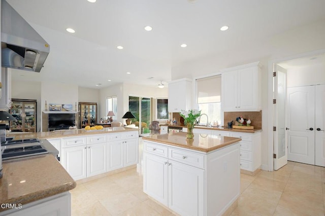 kitchen featuring white cabinetry, a center island, backsplash, kitchen peninsula, and exhaust hood