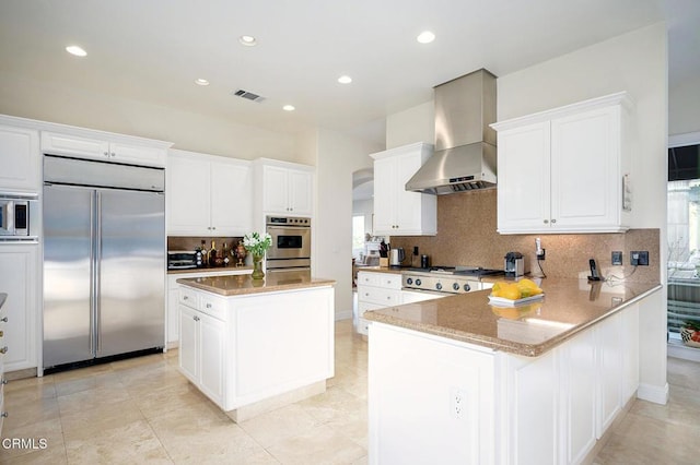 kitchen featuring decorative backsplash, built in appliances, a center island, and wall chimney range hood