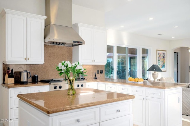 kitchen featuring white cabinets, decorative backsplash, a kitchen island, and wall chimney range hood