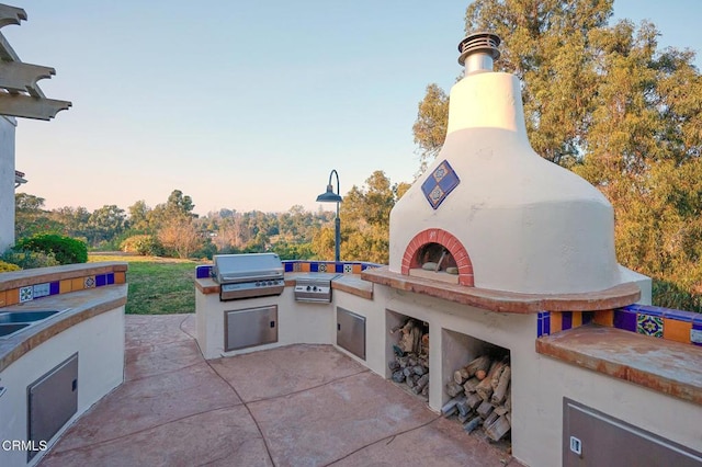 patio terrace at dusk with an outdoor brick fireplace and area for grilling