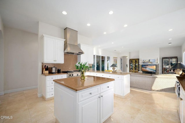 kitchen with white cabinets, a center island, wall chimney range hood, and kitchen peninsula