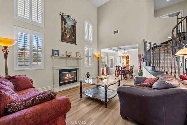 living room featuring a towering ceiling, light hardwood / wood-style floors, and an inviting chandelier