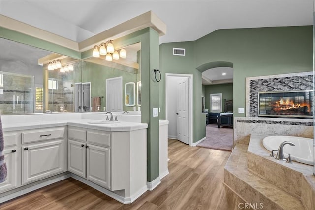 bathroom featuring a wealth of natural light, tiled bath, wood-type flooring, a fireplace, and vanity