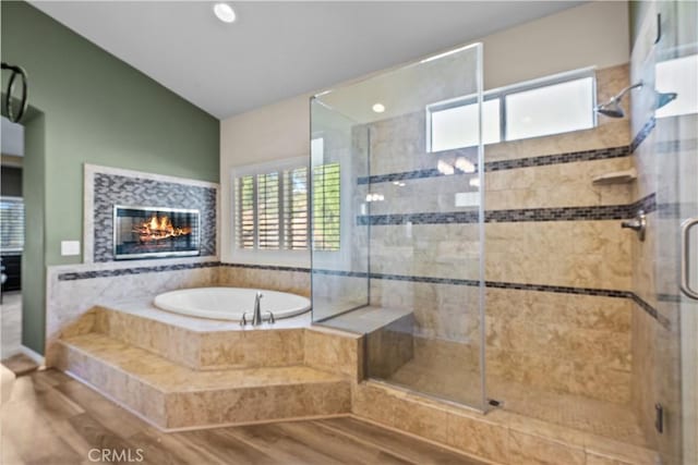 bathroom with hardwood / wood-style floors, a fireplace, shower with separate bathtub, and vaulted ceiling