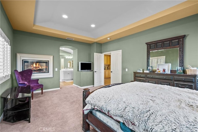 carpeted bedroom featuring a tray ceiling, connected bathroom, and multiple windows